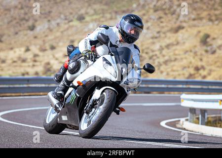 Pilote de moto prenant une courbe au premier plan, avec un fond de nature et de ciel bleu Banque D'Images