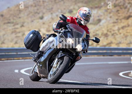 Pilote de moto prenant une courbe au premier plan, avec un fond de nature et de ciel bleu Banque D'Images