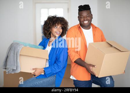 Déménagement à domicile. Heureux couple noir portant des boîtes en carton dans leur nouvelle maison Banque D'Images