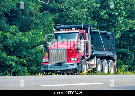 Plan horizontal d'un camion à benne basculante rouge robuste qui rejoint la route principale. Banque D'Images