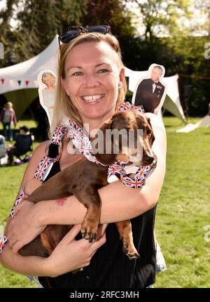 Jeune femme avec son chien et découpes de Camilla Parker Bowles et King Charles 3 pendant le couronnement, Alton, Hampshire, Royaume-Uni. Banque D'Images