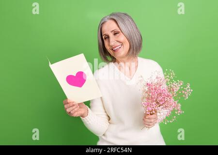 Photo de bonne humeur optimiste souriante dame senior tenir la lecture de sa carte de voeux bonne Saint Valentin isolé sur fond de couleur verte Banque D'Images