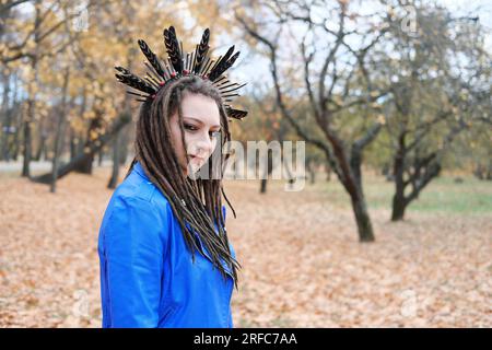 Une femme d'âge moyen en dreadlocks et un cerceau sur ses cheveux en plumes se promène dans le parc d'automne. La femme regarde la caméra. Photo horizontale Banque D'Images