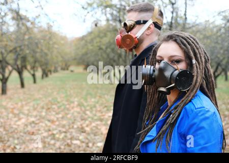 Une femme avec des dreadlocks et un masque à gaz et un homme avec des lunettes steampunk et un masque à gaz posent dans un parc d'automne. Concept de catastrophe écologique. Horizontal Banque D'Images