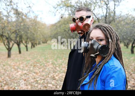 Une femme avec des dreadlocks et un masque à gaz et un homme avec des lunettes steampunk et un masque à gaz posent dans un parc d'automne. Concept de catastrophe écologique. Horizontal Banque D'Images