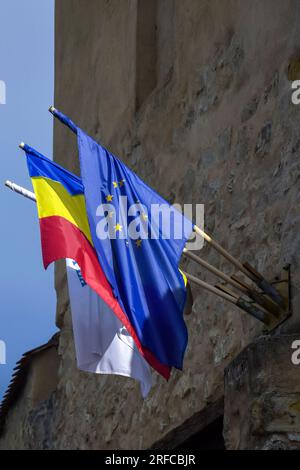 Le drapeau de l'Union européenne et le drapeau roumain sont fixés sur la façade d'une ancienne forteresse de Rupea sur fond de ciel nuageux. Copier l'espace. Mise au point sélective. Banque D'Images