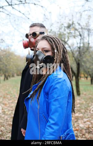 Une femme avec des dreadlocks et un masque à gaz et un homme avec des lunettes steampunk et un masque à gaz posent dans un parc d'automne. Concept de catastrophe écologique. Vertical p Banque D'Images