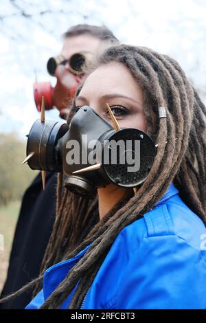 Une femme avec des dreadlocks et un masque à gaz et un homme avec des lunettes steampunk et un masque à gaz posent dans le parc d'automne. Concept de catastrophe écologique. Vertical Banque D'Images