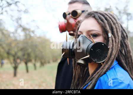 Une femme avec des dreadlocks et un masque à gaz et un homme avec des lunettes steampunk et un masque à gaz posent dans le parc d'automne. Concept de catastrophe écologique. Horizonta Banque D'Images