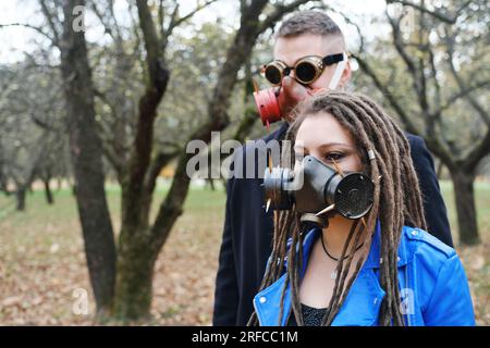 Une femme avec des dreadlocks et un masque à gaz et un homme avec des lunettes steampunk et un masque à gaz regardent la caméra et posent dans le parc d'automne. disa écologique Banque D'Images