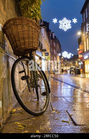 Vélo reposant sur le mur, sur Sliver Street Cambridge, trottoir humide avec des lumières de Noël sur le fond. Banque D'Images