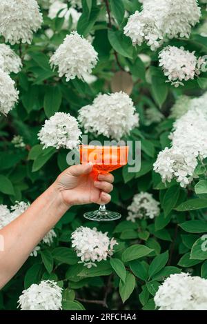 Main féminine tenant le verre avec Spritz Aperol alcool boisson d'été à l'extérieur sur le fond flou de parc vert. Banque D'Images