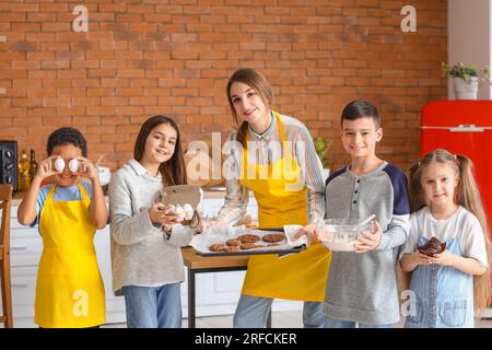 Chef féminin avec groupe de petits enfants et pâtisserie préparée après le cours de cuisine en cuisine Banque D'Images