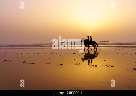 Vue coucher de soleil avec silhouette de chevaux et cavaliers sur la plage d'Essaouira (Mogador), Maroc Banque D'Images