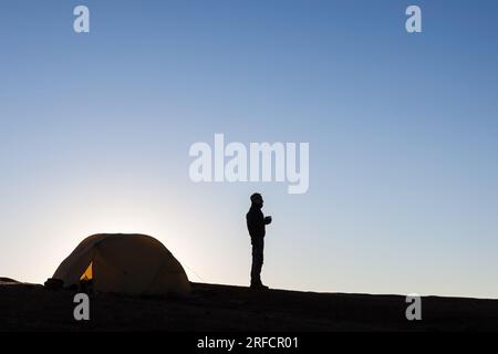 Silhouette de camping d'une tente et d'une fille dans les hautes montagnes de l'Himalaya au Népal. Voyageur seul debout près de la tente de camping regardant à la distance. Banque D'Images