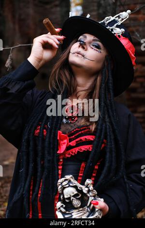 Une femme en forme de Baron Saturday avec un cigare à la main. Le modèle est habillé d'un corset, d'un cardigan et d'un chapeau haut de gamme décoré de figuier squelette Banque D'Images