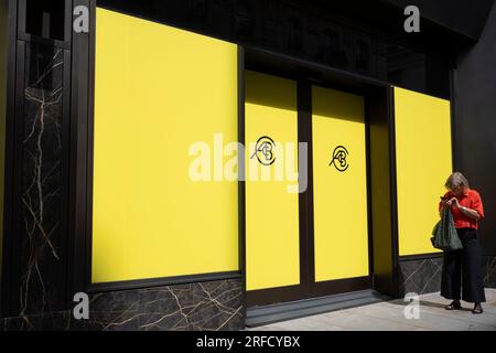 Une personne passe devant la palissade jaune pour un prochain showroom de voitures Lotus sur Piccadilly dans le West End de la capitale, le 25 juillet 2023, à Londres, Angleterre. Banque D'Images