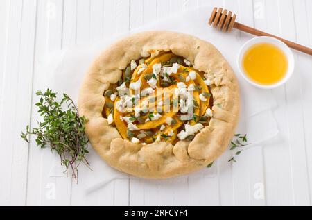 Galette maison avec citrouille, fromage feta, miel, graines de citrouille et thym sur fond blanc, vue de dessus. Banque D'Images