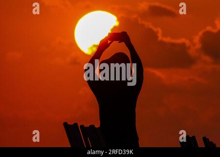 Île de Palms, États-Unis. 02 août 2023. Un touriste soulève son téléphone photo au-dessus de sa tête pour photographier le lever du soleil lors d'une autre journée chaude et bruyante dans le pays bas, le 2 août 2023 à l'île de Palms, en Caroline du Sud. Une vague de chaleur prolongée dans le sud des États-Unis continue d'apporter un temps extrêmement chaud et humide à la région. Crédit : Richard Ellis/Richard Ellis/Alamy Live News Banque D'Images