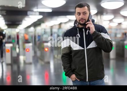 Homme en veste avec un téléphone portable près du tourniquet dans le métro Banque D'Images