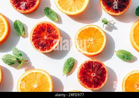 Divers agrumes tranchés, oranges rouges avec des feuilles de menthe verte sur un fond blanc avec des ombres dures. Vue de dessus, pose à plat. Banque D'Images