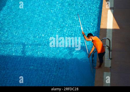 Vue de dessus d'un ouvrier nettoyant une piscine dans une maison privée en été. Banque D'Images