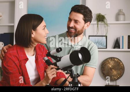 Couple heureux utilisant le télescope pour regarder les étoiles dans la chambre Banque D'Images