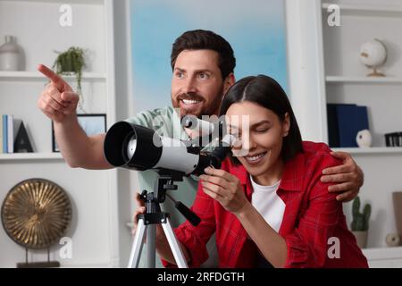 Couple heureux regardant les étoiles à travers le télescope dans la chambre Banque D'Images