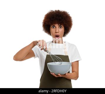 Jeune femme émotionnelle dans le tablier tenant le bol et fouetter sur fond blanc Banque D'Images