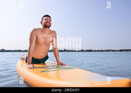 Homme pratiquant le yoga sur la planche de SUP sur la rivière Banque D'Images