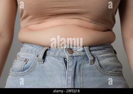 Femme en surpoids en jeans serrés sur fond gris, gros plan Banque D'Images