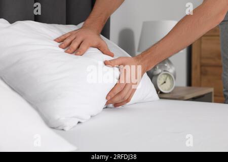 Homme ajustant l'oreiller sur le lit à la maison, closeup Banque D'Images