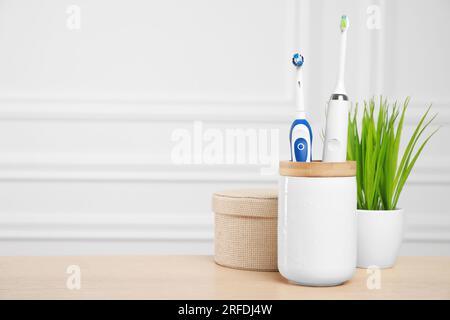 Brosses à dents électriques dans le support sur la table en bois. Espace pour le texte Banque D'Images