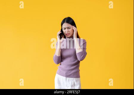 Une femme asiatique stressée et insatisfaite parle au téléphone avec quelqu'un, se sentant confuse et incertaine à propos de quelque chose. fond jaune isolé. Banque D'Images