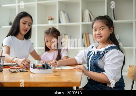 Une adorable jeune fille asiatique est assise dans la salle de classe avec un professeur et ses amis, souriant et regardant la caméra. Enfants, école primaire St Banque D'Images