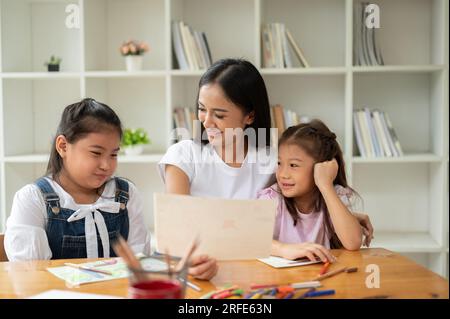 Une jeune fille asiatique heureuse et gentille baby-sitter ou professeur privé enseigne l'art aux jeunes enfants. professeur, tuteur privé, sœurs Banque D'Images