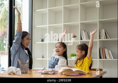 Deux petites filles asiatiques heureuses et joyeuses et une enseignante gentille lèvent la main après la fin du cours. préscolaire, maternelle, élément Banque D'Images