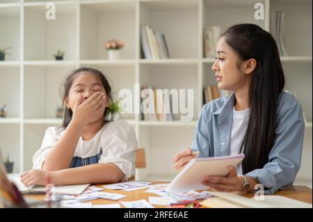 Une belle et gentille enseignante asiatique ou un tuteur privé parle et convainc une fille paresseuse endormie d'étudier et de faire attention à une leçon. Banque D'Images