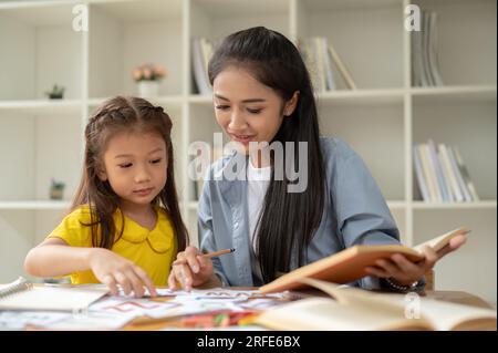 Une adorable petite fille d'âge préscolaire asiatique se concentre sur l'étude des cartes-éclair de l'alphabet anglais avec un professeur particulier gentil à la maison. Enfants et éducation co Banque D'Images