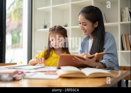 Une maman attentionnée aidant et enseignant l'anglais à sa petite fille à la maison. Famille heureuse, baby-sitting, école à domicile, professeur privé Banque D'Images