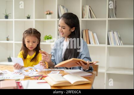 Une jolie fille d'âge préscolaire asiatique étudie l'alphabet anglais sur des flashcards avec une enseignante gentille et attentionnée. apprendre, étudier, développer l'enfant Banque D'Images