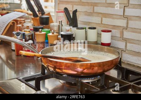 Le lait et les oignons hachés sont frits dans une casserole en cuivre sur un feu à gaz. Banque D'Images