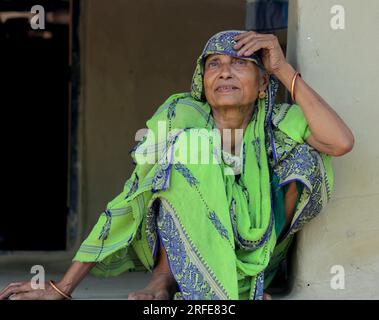 Une femme indienne de 70 ans assise sur le sol avec du saree vert. Une journée normale dans la vie de village indien. Banque D'Images