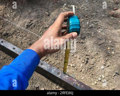 Le constructeur utilise un mètre à ruban pour trouver la distance entre le sol et le moule afin de trouver les coordonnées correctes pour préparer le plancher de ciment. Flou Banque D'Images