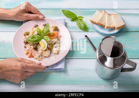Les mains féminines servent une assiette de riz froid, garnie d'œufs durs, d'olives, de tomates, de fromage et de feuilles de basilic Banque D'Images