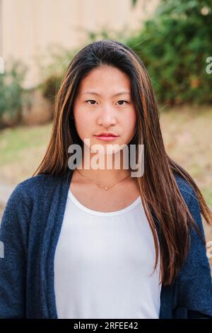 Portrait individuel vertical de jeune femme sérieuse debout dehors. Une adolescente pensive regardant la caméra. Vue de face d'une jeune femme chinoise. Plan de tête d'une fière adolescente écolière. Photo de haute qualité Banque D'Images