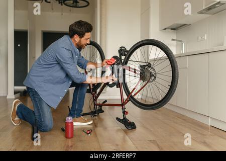 Concentré bel homme dans des vêtements décontractés réparant le vélo lui-même à la cuisine à la maison Banque D'Images