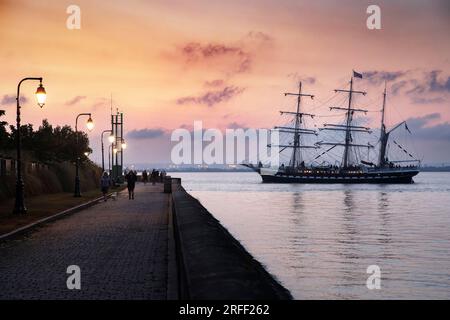 France, Calvados, Honfleur, Armada 2023, Grand Parade, La barque Belem à trois mâts navigue devant la digue où se tiennent quelques spectateurs, au soleil couchant Banque D'Images