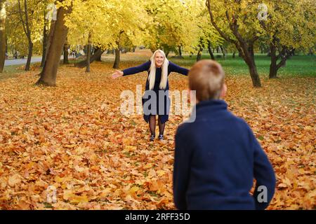 Mère et fils jouent ensemble dans le parc d'automne. Le garçon court vers sa mère, sa mère doit l'attraper Banque D'Images