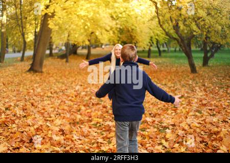 Mère et fils jouent ensemble dans le parc d'automne. Le garçon court vers sa mère, sa mère doit l'attraper Banque D'Images